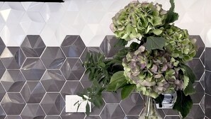 Eine Küche mit einer zurückliegenden Wandfläche aus sechseckigen Fliesen, einem Gasherd und einer Vase mit grünen Blumen auf der Arbeitsplatte.