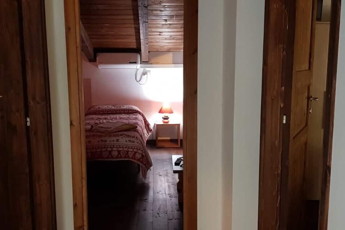 A narrow hallway leading to a bedroom with a bed and a bedside table with a lamp.