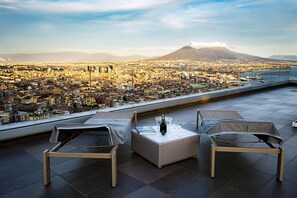 A rooftop terrace with two lounge chairs, a table with a bottle and glasses, and a panoramic city view with a mountain in the distance. - Terrazza Manù ... Naples at your feet ... (Napoli)