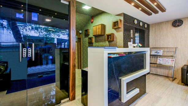 A reception area with a glass door, a reception desk, a clock, and a newspaper rack. - Treebo Trend Blue Bells Residency (Mumbai)