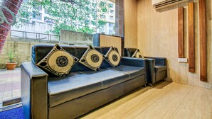 A black leather sofa with decorative pillows, a potted plant, and a view of a building through a window. - Treebo Trend Blue Bells Residency (Mumbai)