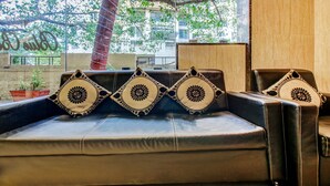 A leather sofa with decorative pillows and a view of a tree and building outside. - Treebo Trend Blue Bells Residency (Mumbai)