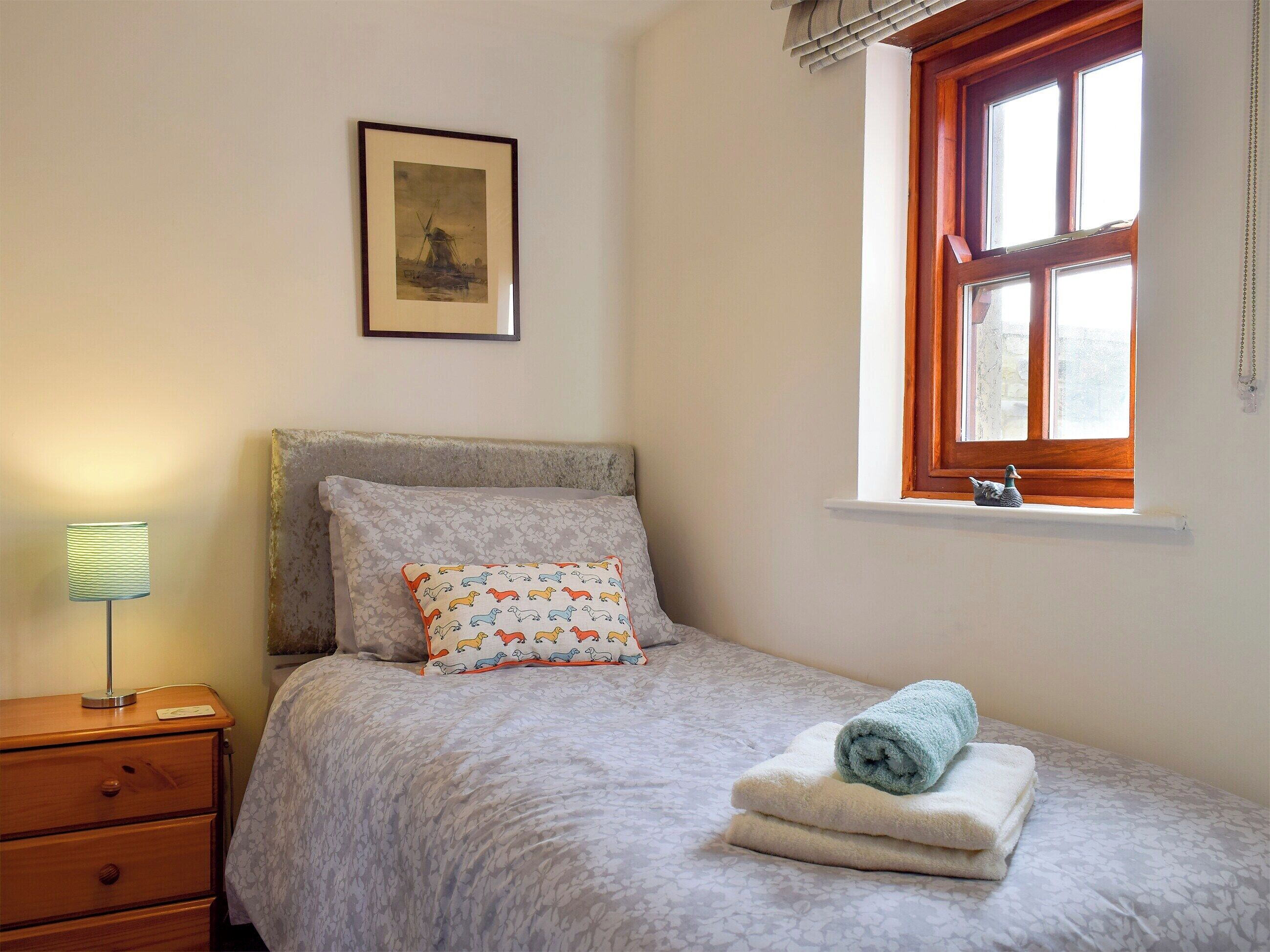 A bedroom with a bed, a nightstand, a lamp, a window with a view, and a framed picture on the wall.