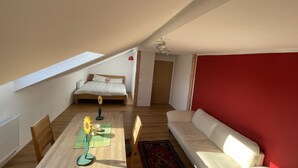 A bedroom with a bed, a wooden headboard, a red wall, a white sofa, and a dining table with a sunflower decoration. - Cozy vacation apartment "Schwalbennest" under the roof with garden access (Bundenthal)