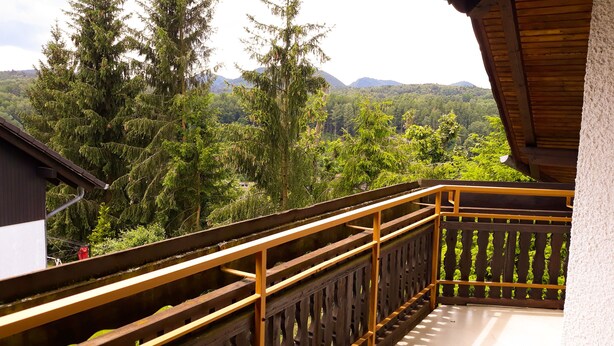 A balcony with a wooden railing overlooking a forested area with mountains in the distance. - Cozy vacation apartment "Schwalbennest" under the roof with garden access (Bundenthal)