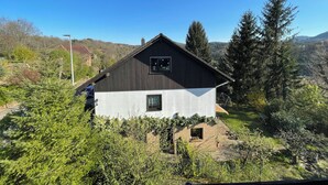 A modern house with a sloped roof, surrounded by lush greenery and trees. - Cozy vacation apartment "Schwalbennest" under the roof with garden access (Bundenthal)