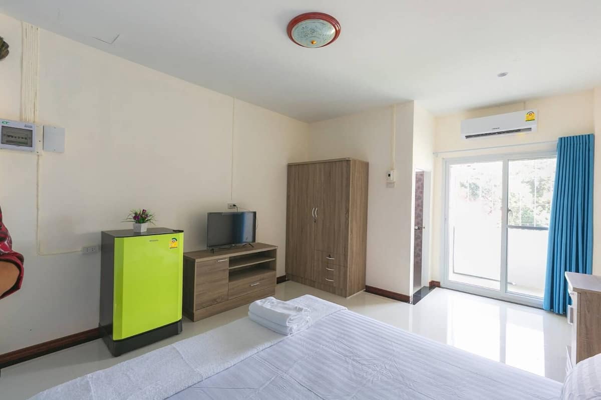 Una habitación de hotel con cama, televisor en un soporte, armario, refrigerador pequeño y puerta corrediza de vidrio al exterior.