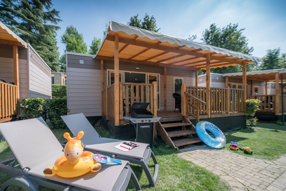 Ein Ferienhaus mit überdachter Veranda, Grill und Poolbereich.