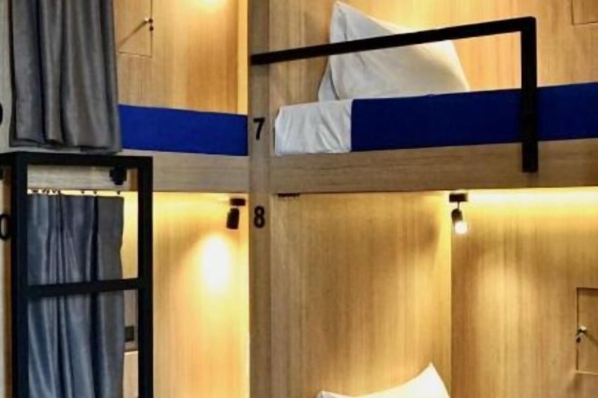 A bunk bed room with wooden walls and a blue stripe. There are curtains on the windows and a door.