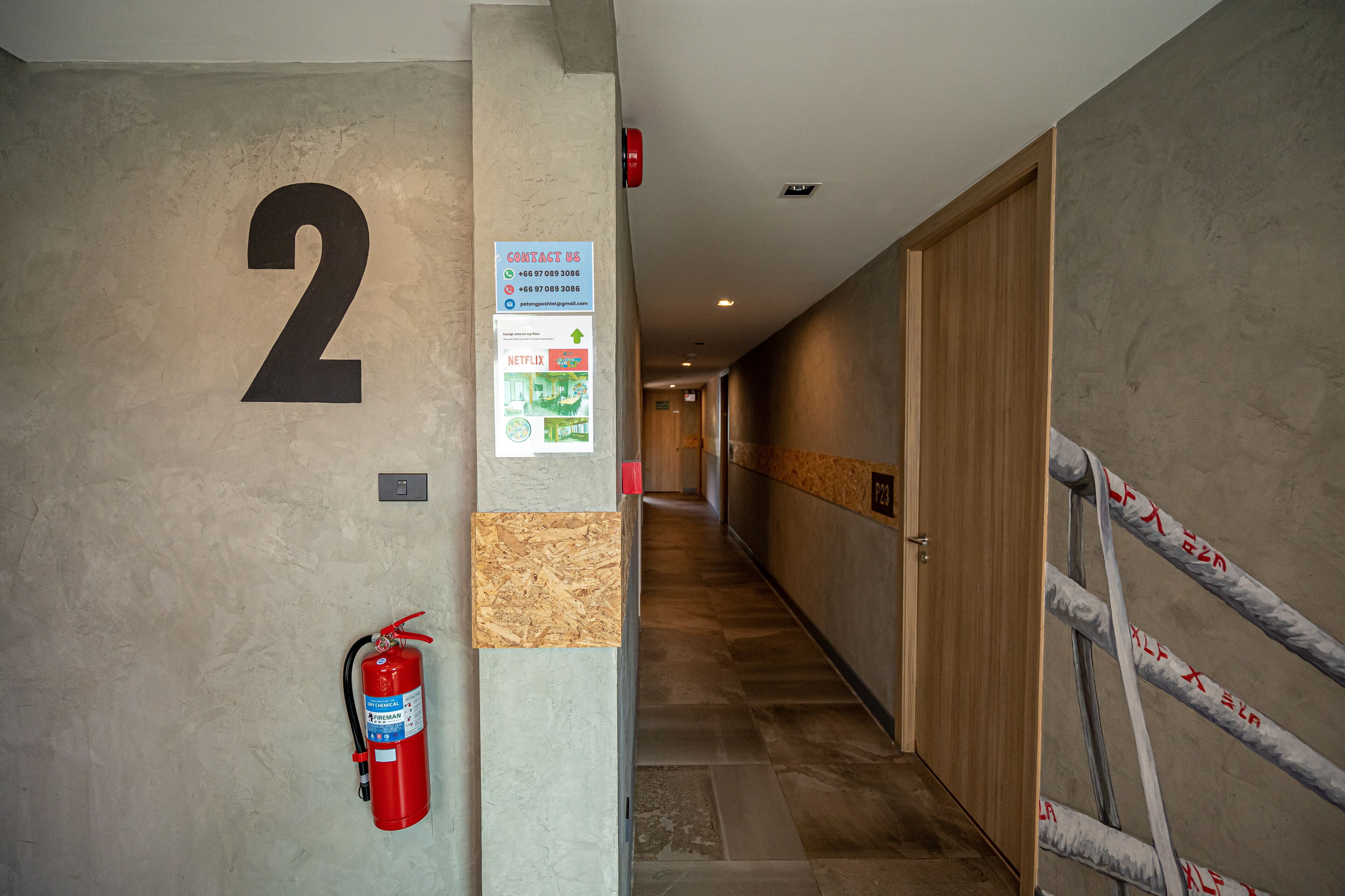 Un couloir avec un grand numéro « 2 » peint sur le mur, un extincteur et une affiche indiquant les coordonnées à contacter.