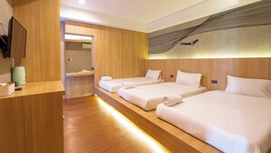 Ein Hotelzimmer mit drei Betten, Holzboden, einem Empfangstresen und einem an der Wand befestigten Fernseher.