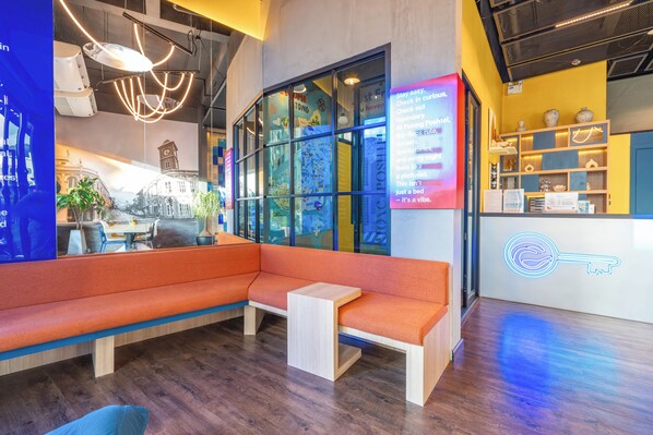 A modern hotel lobby with a seating area, a digital display, and a reception desk. - Patong Poshtel - Adults Only - Hostel (Patong)