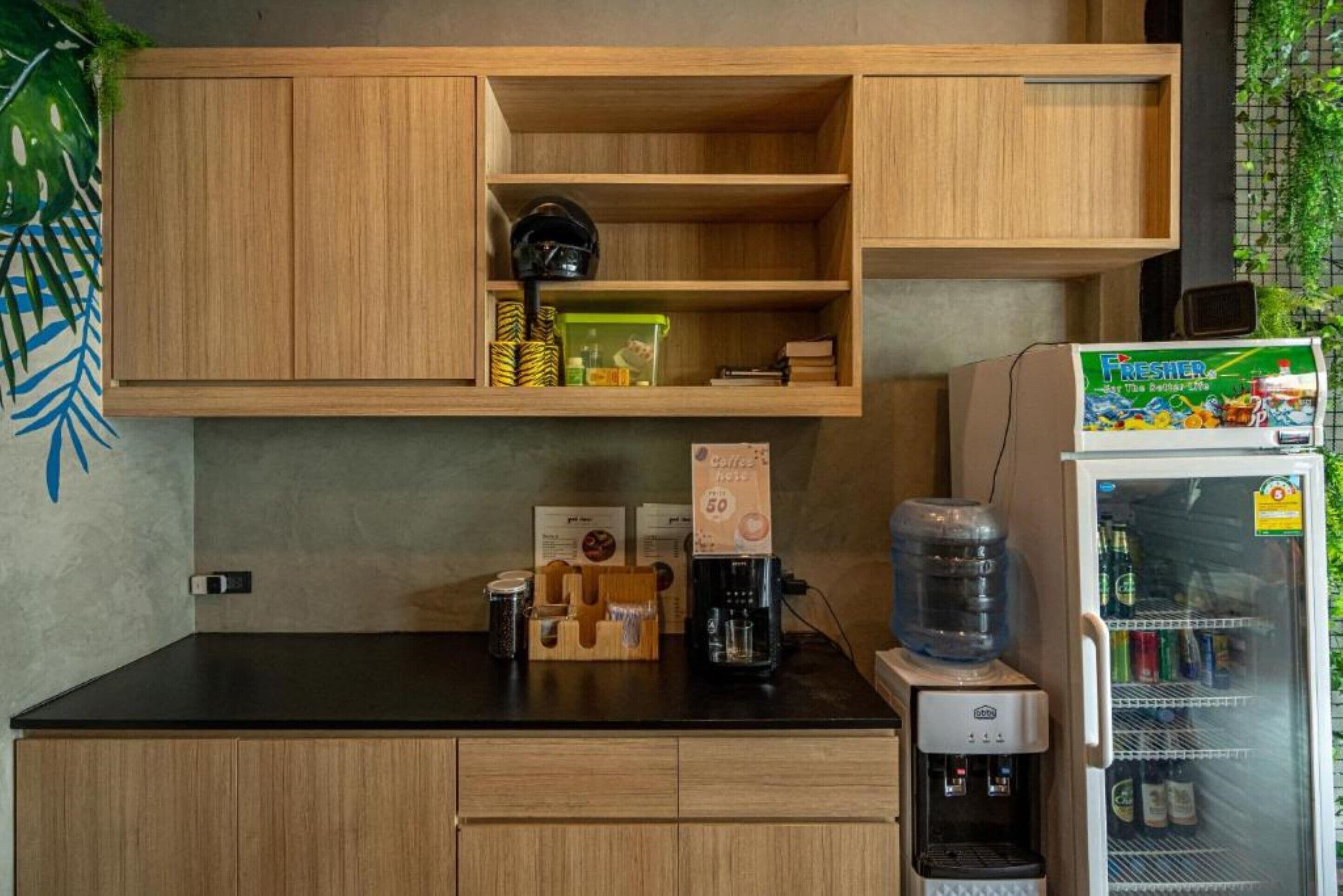 A kitchenette with wooden cabinets, a coffee machine, a water dispenser, and a refrigerator stocked with beverages.
