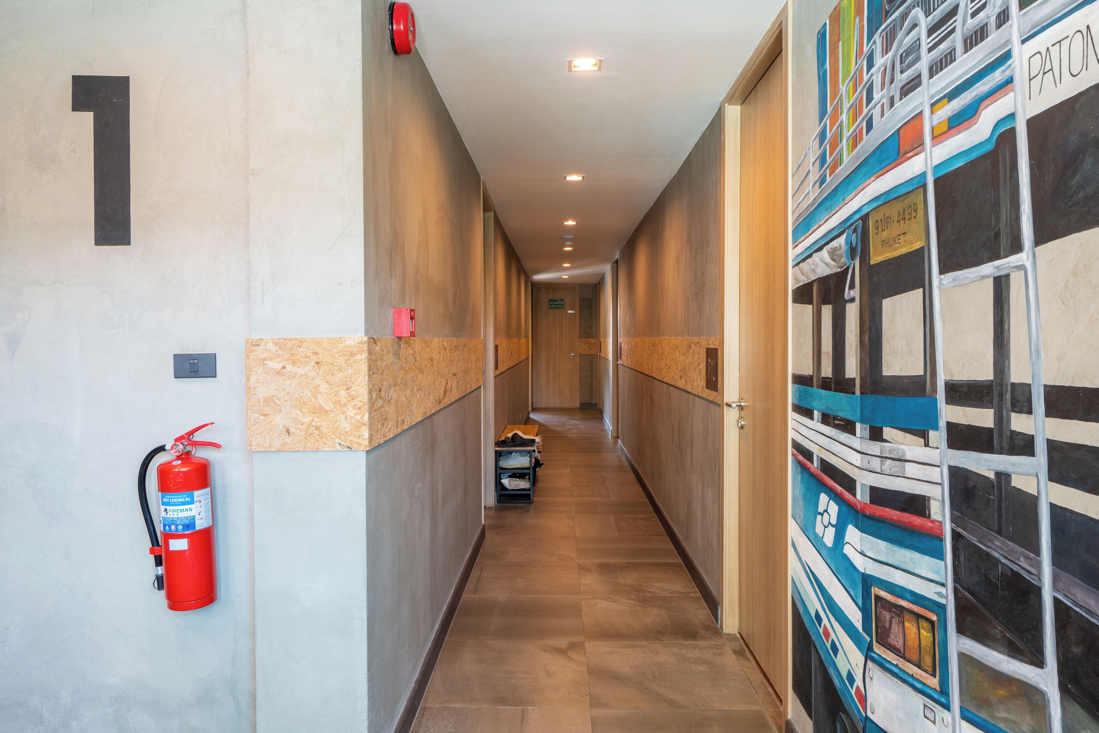 A hallway with a fire extinguisher mounted on the wall, a number '1' sign, and a mural depicting a train.