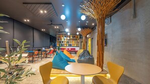 Ein moderner Lounge-Bereich mit gelben Sesseln, einem runden Tisch und einer Sitzecke mit orange- und blauen Kissen.