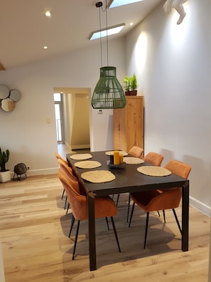 A dining area with a long table, orange chairs, and a green pendant light.