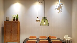 Un coin repas comprenant un buffet en bois, une table avec des chaises orange et des lampes suspendues.