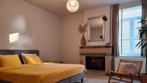 Une chambre à coucher avec un lit, une chaise, une cheminée et une fenêtre avec des rideaux.
