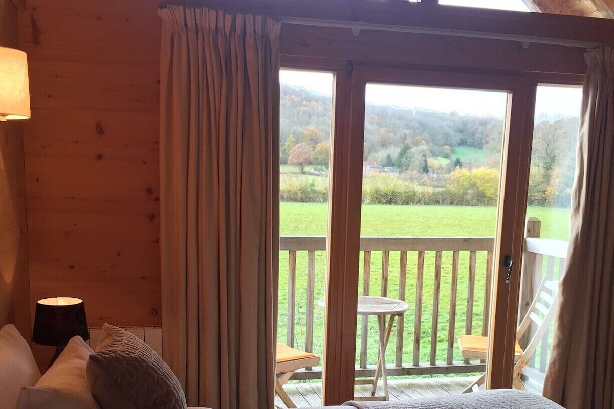A bedroom with a large bed, wooden walls, and a balcony with a view of the countryside.