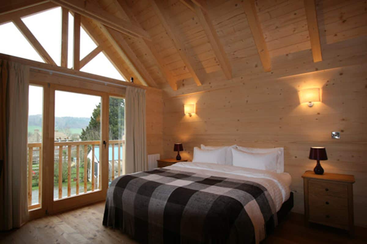 A wooden cabin bedroom with a large bed, two bedside tables, and a balcony with a view of the outdoors.