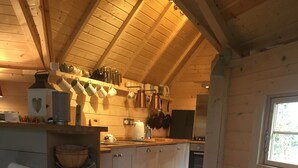 A cozy cabin interior with a wooden ceiling, a kitchen area with various appliances, a white sofa, and a patterned rug. - Pandy B&B (Hereford)