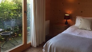 A bedroom with a bed, a nightstand, a lamp, a window with curtains, and a view of greenery outside. - Pandy B&B (Hereford)