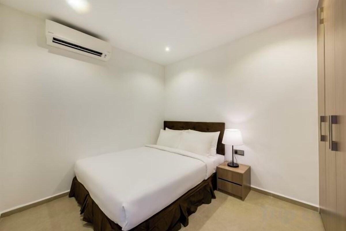 Een slaapkamer met een bed, nachtkastje, lamp, kledingkast en airconditioning.