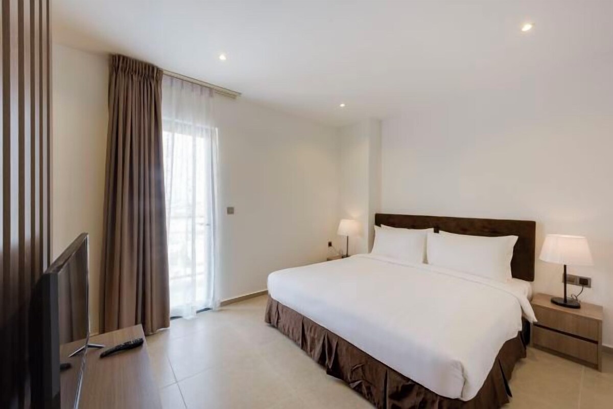 Una habitación de hotel con una cama grande, dos lámparas de noche, un televisor y una ventana con cortinas.