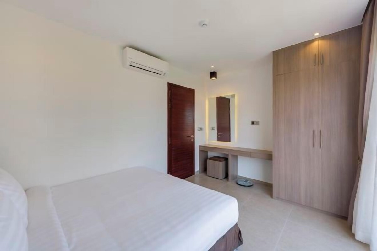 Habitación de hotel moderna con una cama, un armario de madera, una tocadora con espejo y un equipo de aire acondicionado en la pared.