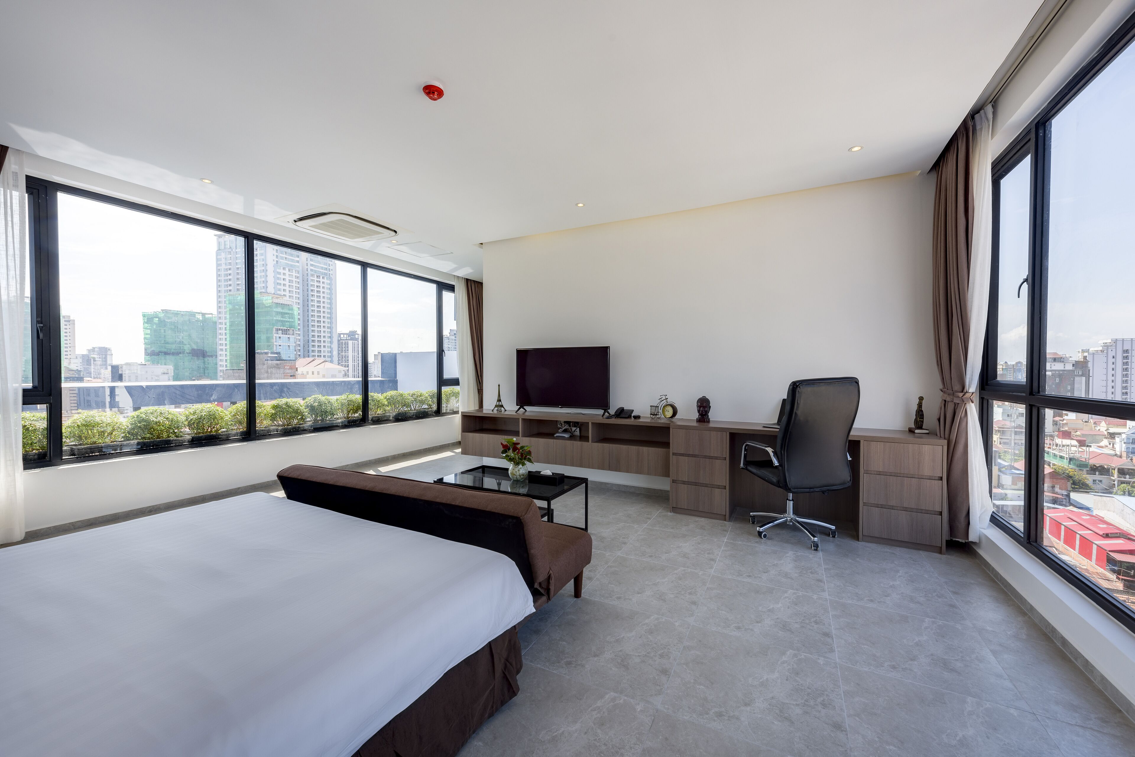 A modern hotel room with a large bed, a desk, a chair, a television, and a view of the cityscape.