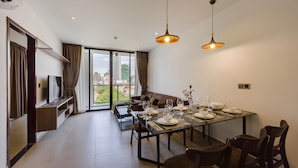 A modern dining area with a large table set for six, a sofa, and a TV on a wall unit.