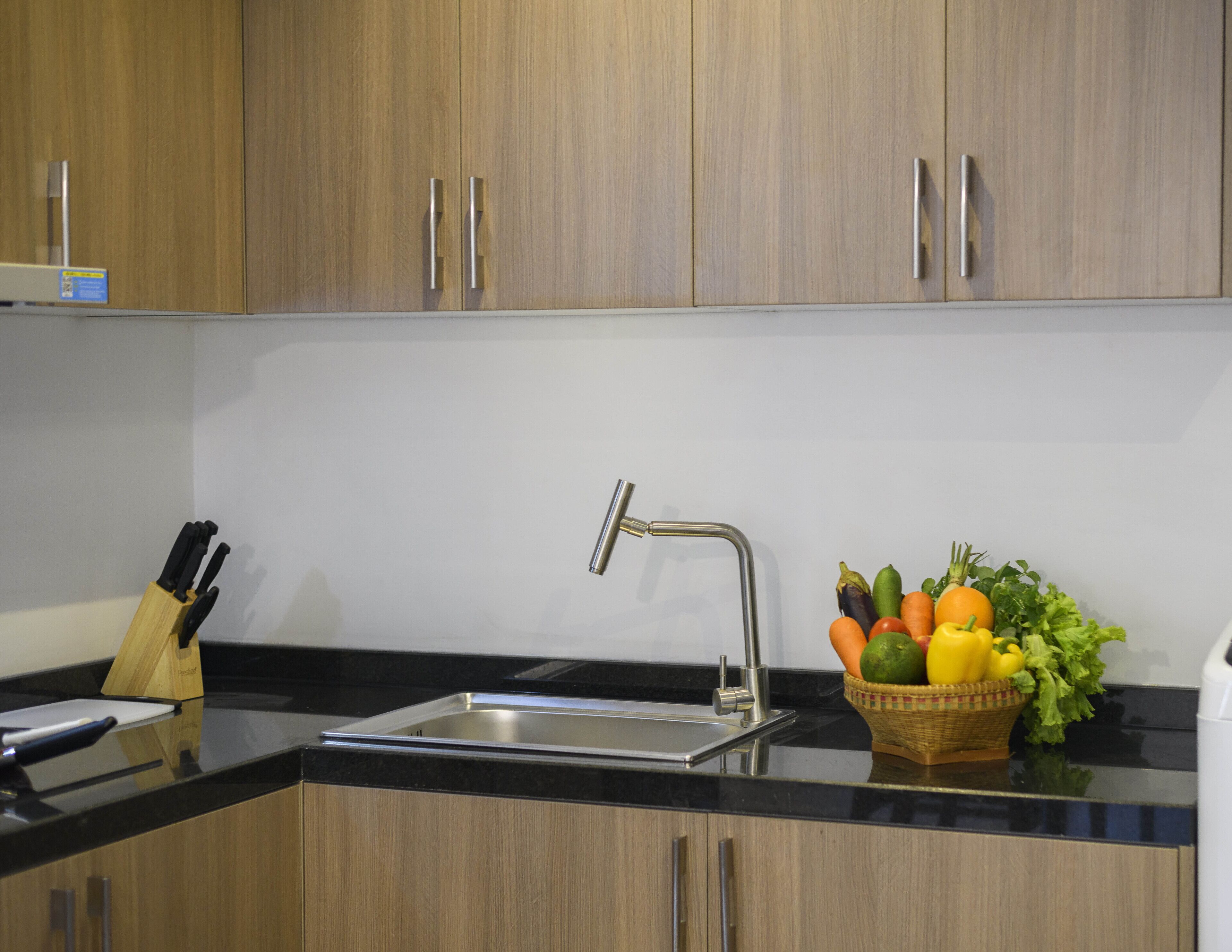 A kitchen with wooden cabinets, a stainless steel sink, and a fruit basket on the counter.