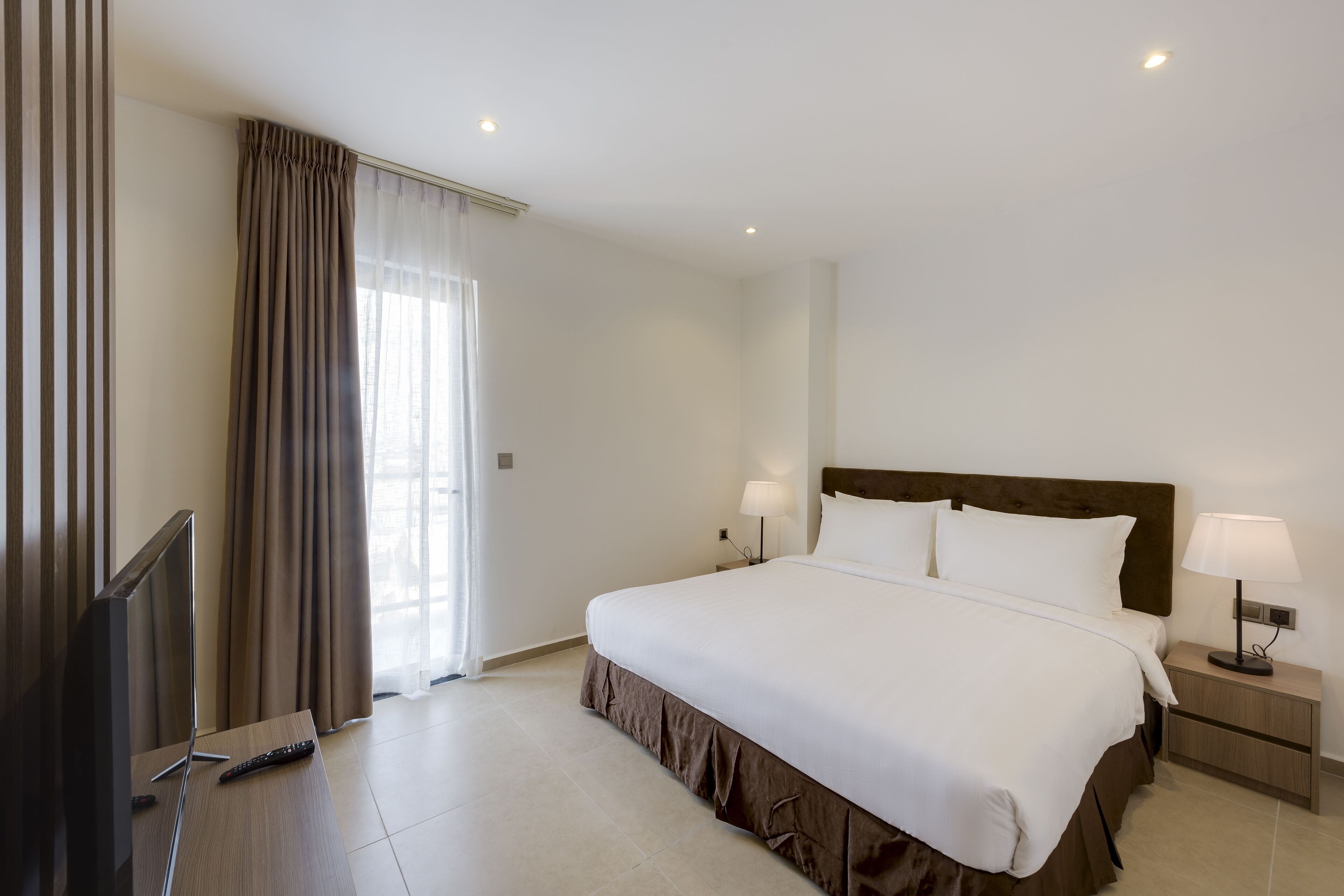 A hotel room with a large bed, two bedside lamps, a TV, and a remote control on the floor.