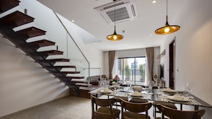 A dining area with a glass table set for four, a staircase, and a large window with curtains.