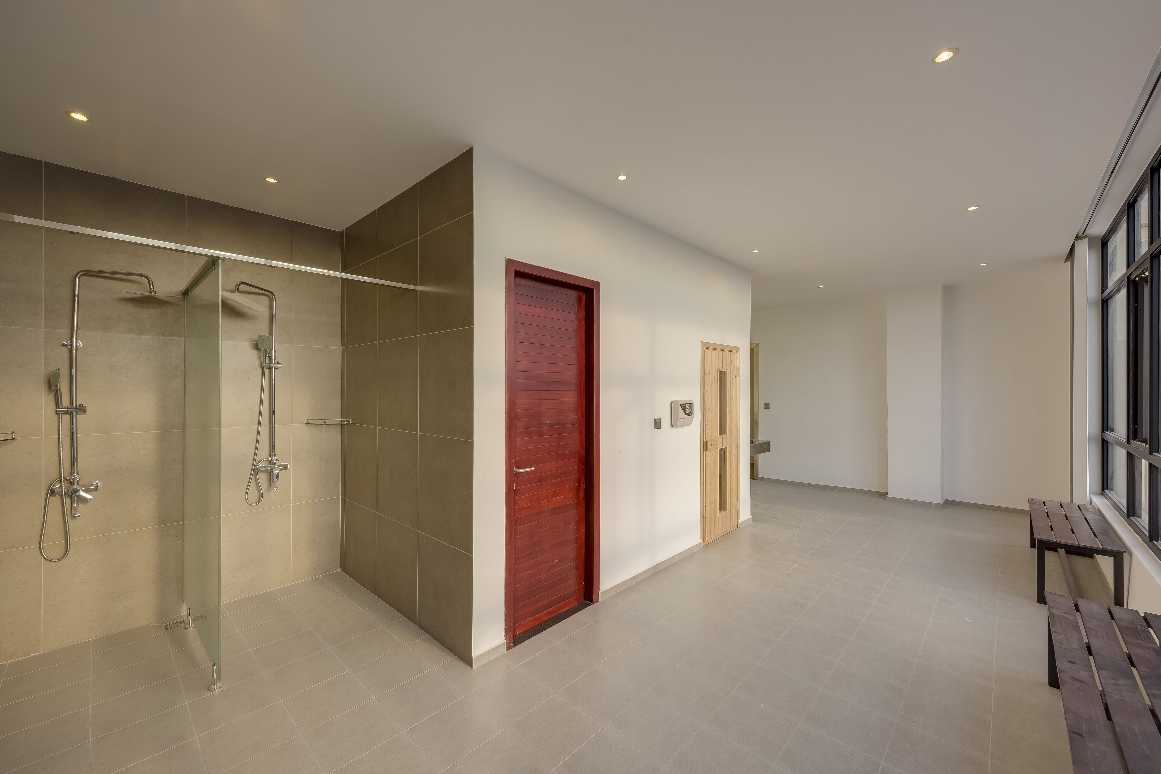 A modern bathroom with a glass shower enclosure, a wooden door, and a bench by the window.