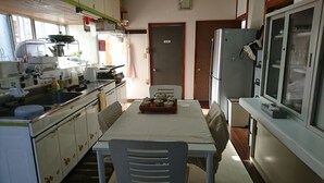 A compact kitchen with basic appliances, a dining table, and a refrigerator. - Free parking, free pets, free cleaning (糸満市)