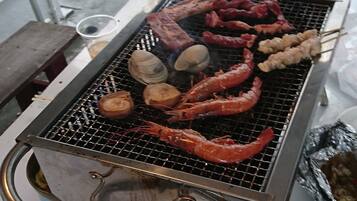 A portable grill with various meats and seafood being cooked.