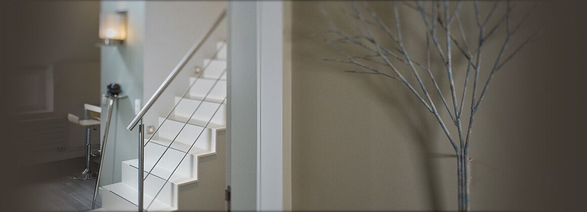 Una escalera con barandilla de metal, un aplique de pared y una rama decorativa en la pared.