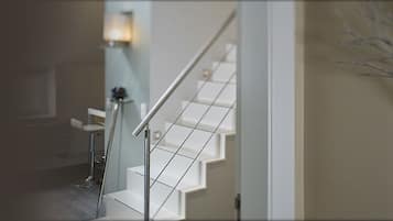 Una escalera con barandilla de metal, un aplique de pared y una rama decorativa en la pared.