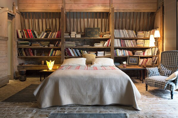 Un dormitorio acogedor con una cama grande, una silla y una estantería llena de libros.