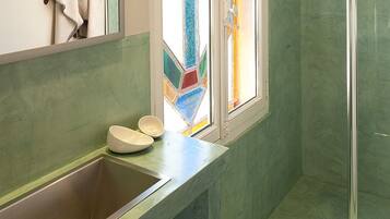 Un baño con una pared verde, un lavabo, un espejo y una ducha.