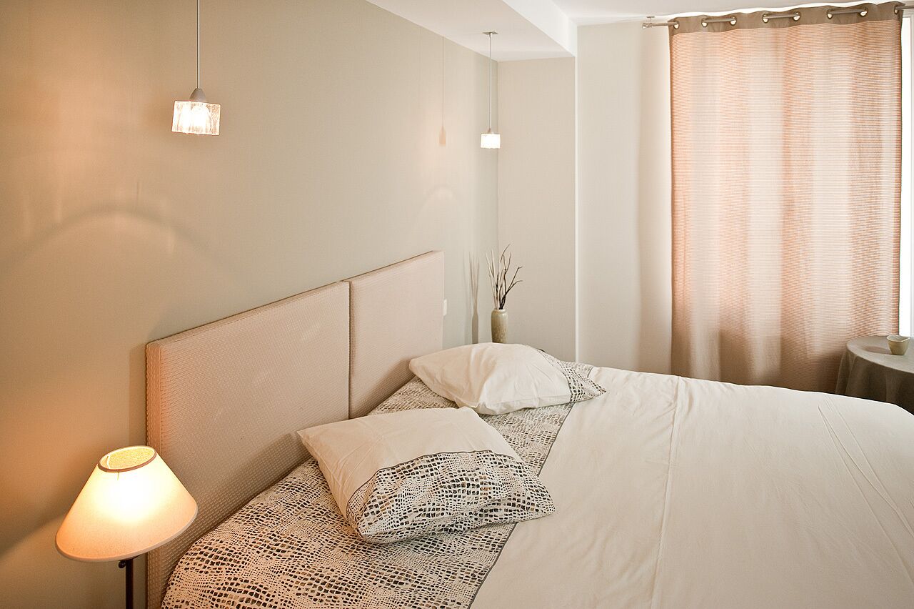 A neatly made bed with a headboard, a bedside lamp, and a vase with branches on the nightstand.