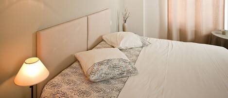 A neatly made bed with a headboard, a bedside lamp, and a vase with branches on the nightstand.