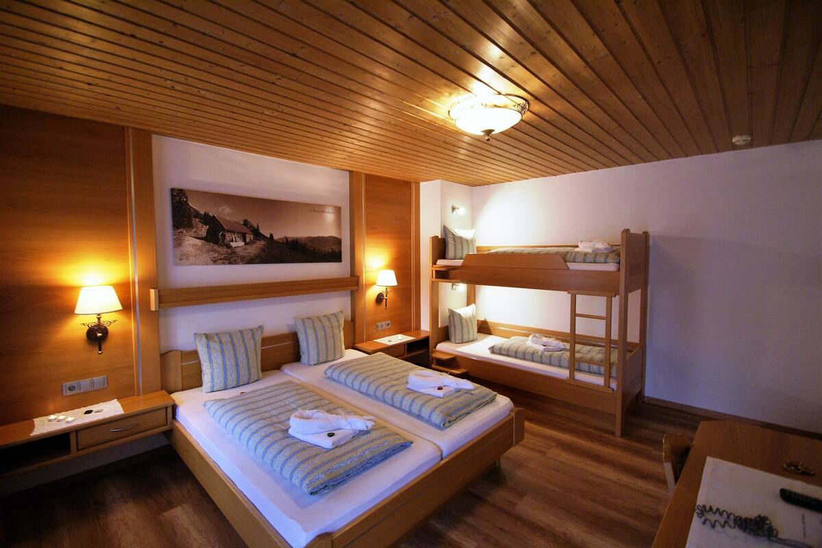 Een hotelkamer met twee bedden, een stapelbed, houten wanden en een plafondlamp.