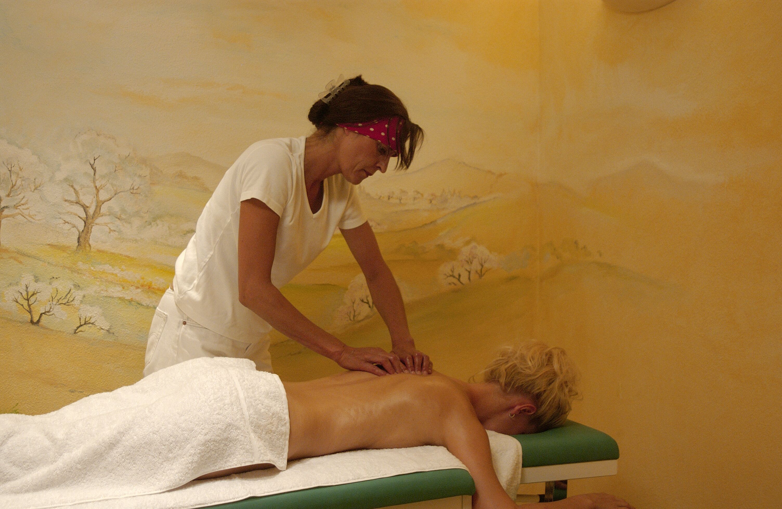 A massage therapy session in a room with a mural of a landscape.
