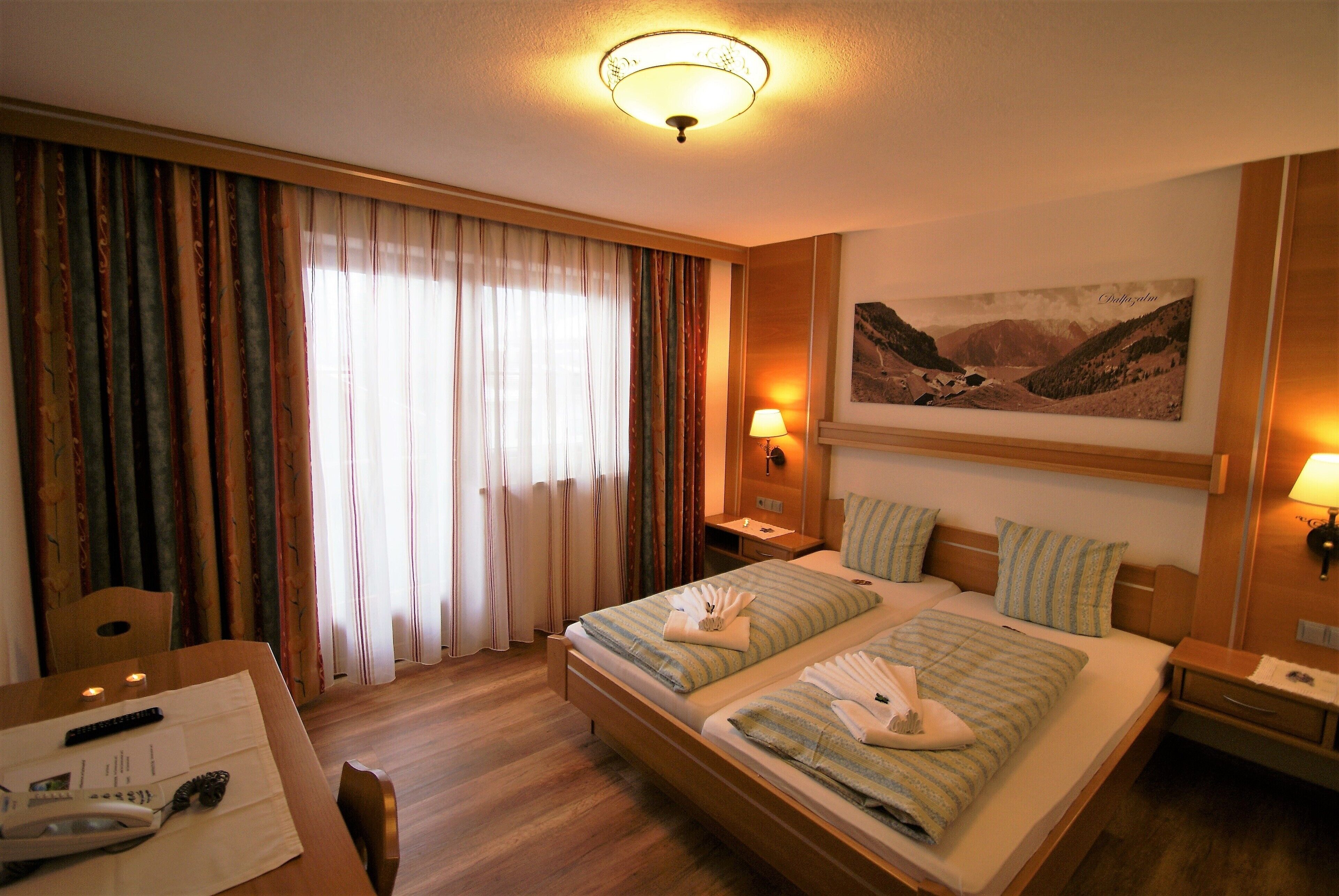 A hotel room with a bed, two bedside tables, a desk with a chair, a telephone, and a painting on the wall.