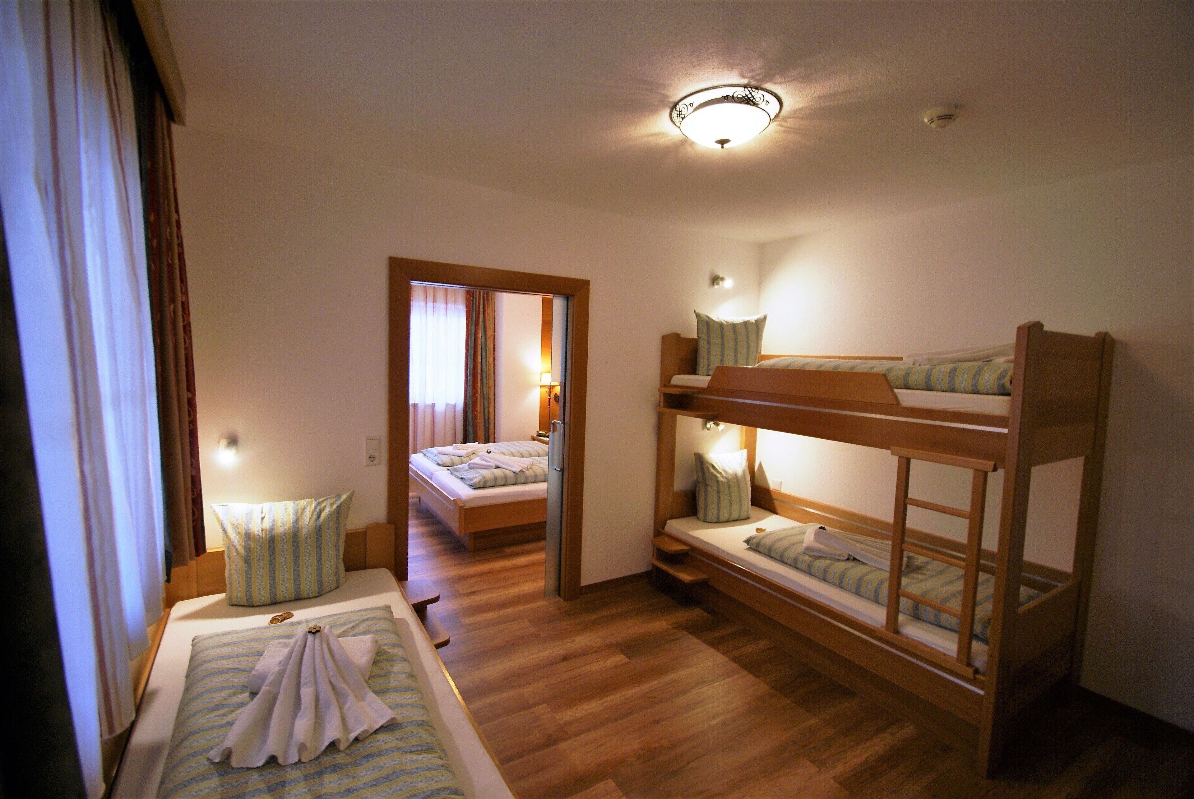 A room with bunk beds, a small desk, and a door leading to another room.