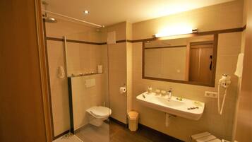 A modern bathroom with a glass-enclosed shower, a toilet, a sink with toiletries, and a mirror.
