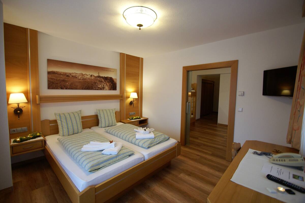 Een hotelkamer met twee bedden, houten vloeren, een wandtelevisie en een schilderij aan de muur.