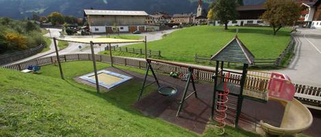 A playground with a slide and swings, surrounded by a fence, with a mountain backdrop.
